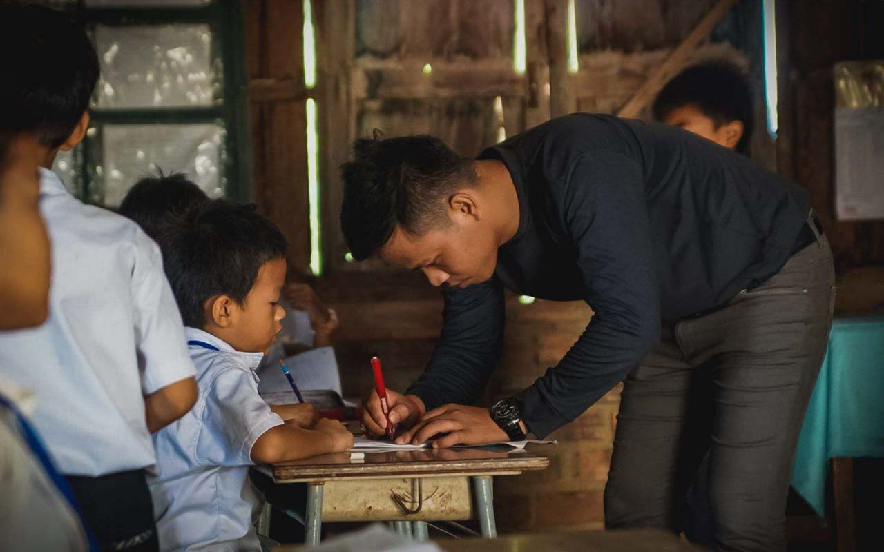 a Cambodian teacher grading papers in a classroom