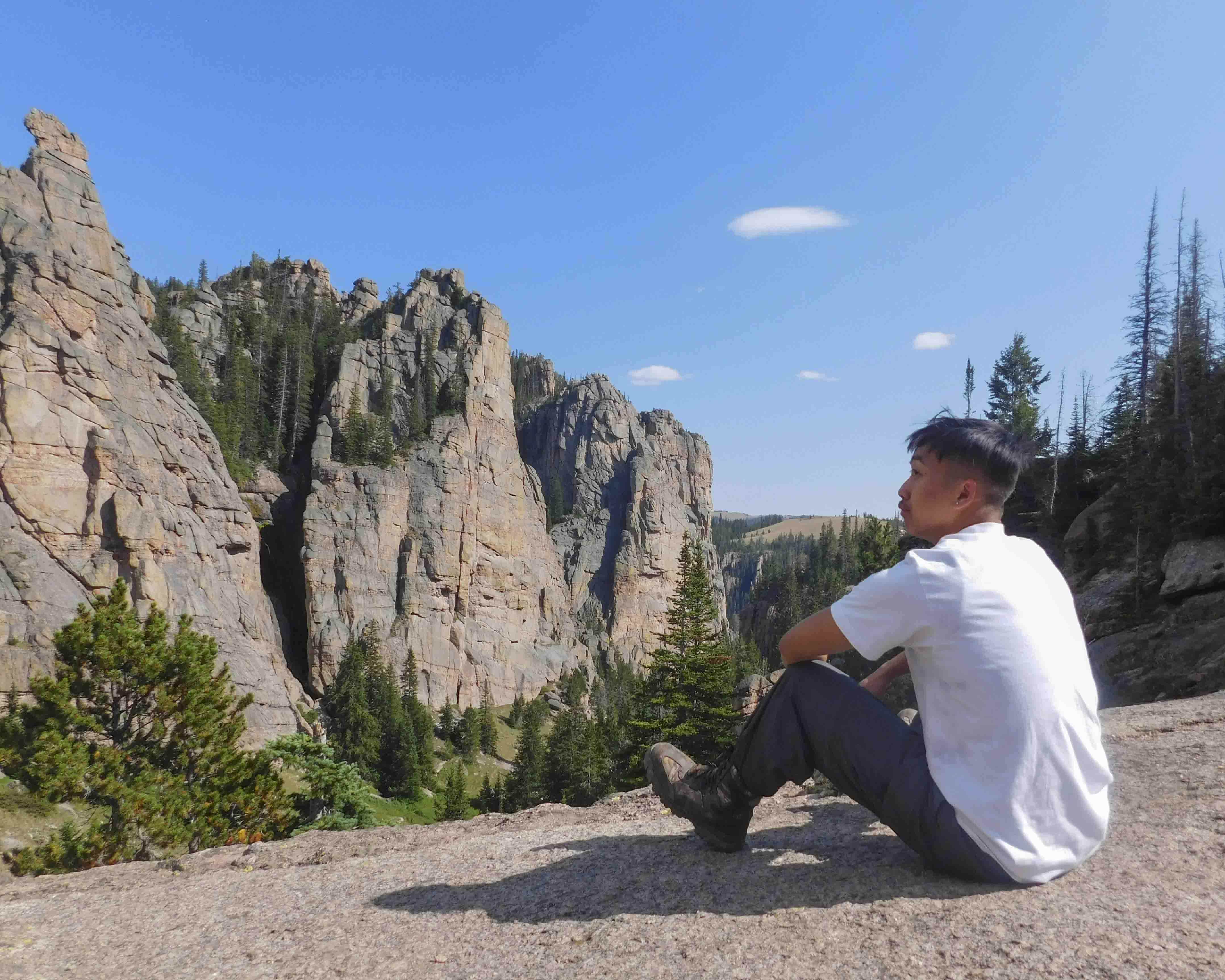 teenage boy sits on large rock slab and looks out at cliffs on community service trips to the Northern Cheyenne