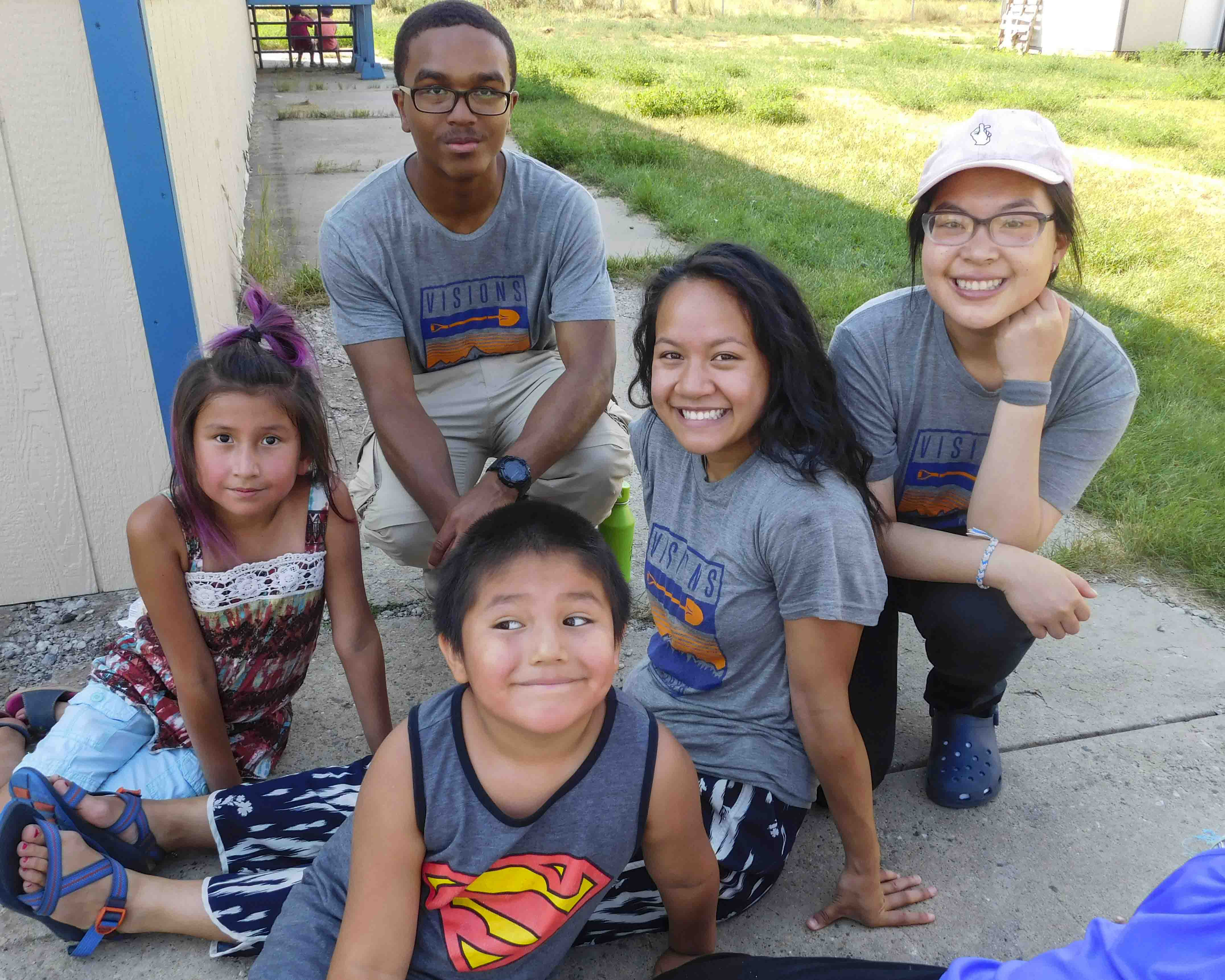 Teen volunteers sit in the shade with local kids on community service trips to the Northern Cheyenne