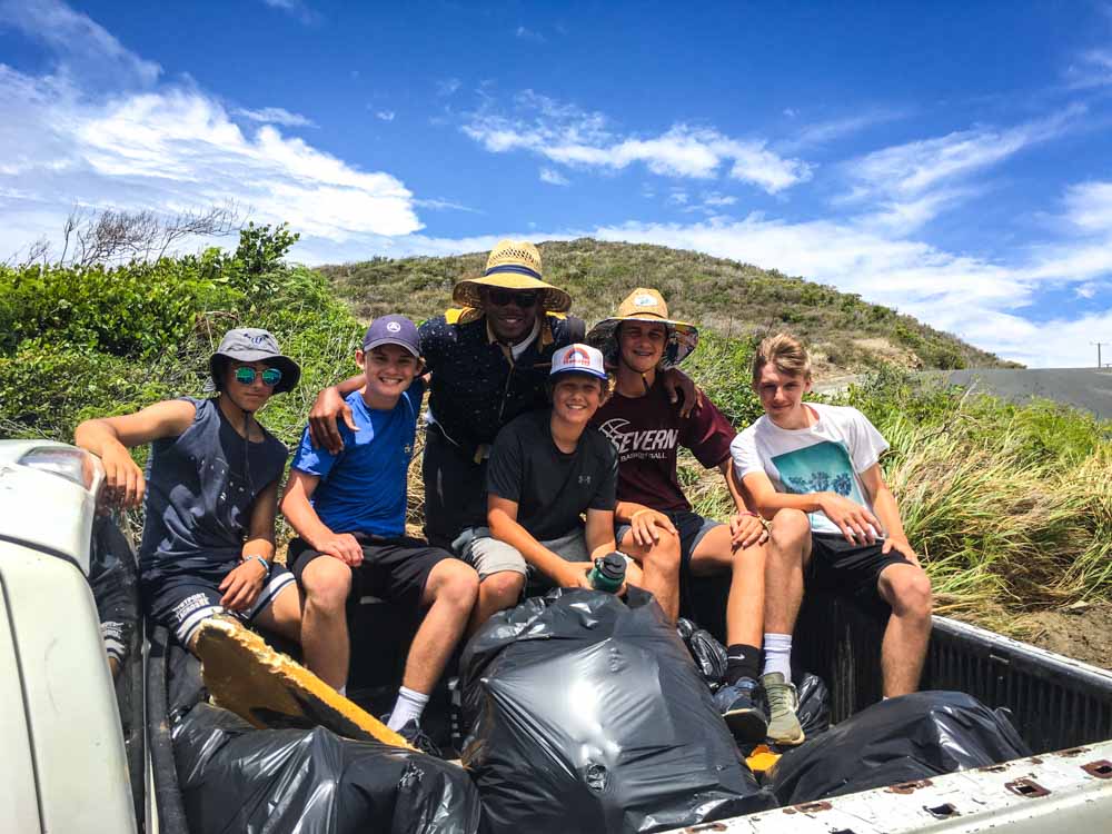 Teenage volunteers sitting in the back of a pickup truck with bags of garbage the cleaned from beaches.