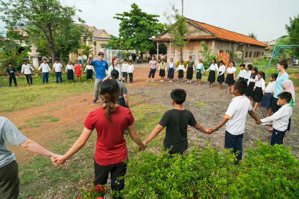 Cambodian students hold hands in a circle to play a game with teen volunteers.