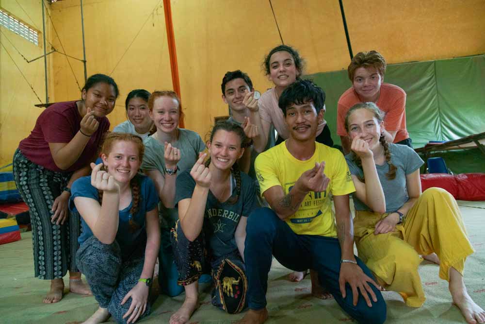 Teen volunteers learn a hand gesture from a Cambodian community member.