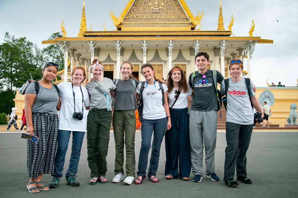 Teen volunteers standing in front of an elaborately decorated Cambodian building.