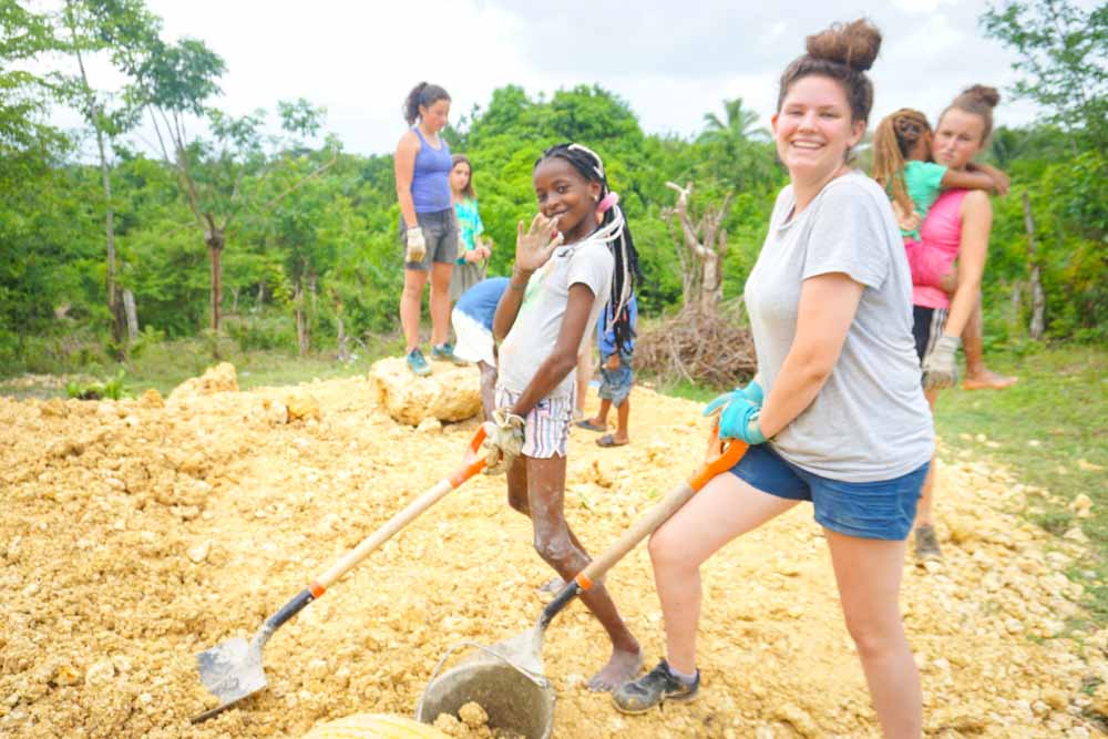 Teen volunteers and community members digging side by side on a summer service project.