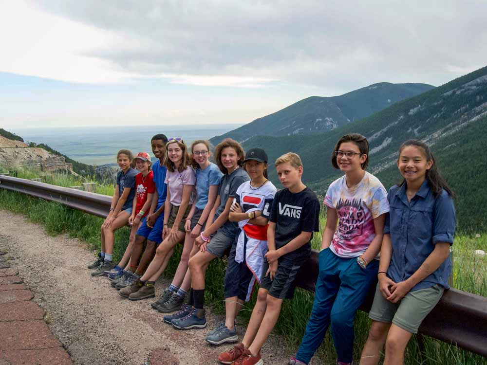 Middle schooler volunteers pose by the roadside for a group photo with mountains.