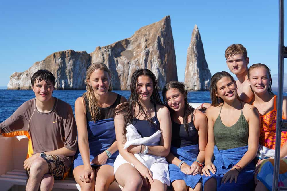 Smiling teens enjoy a boat ride with rock formations in the background.