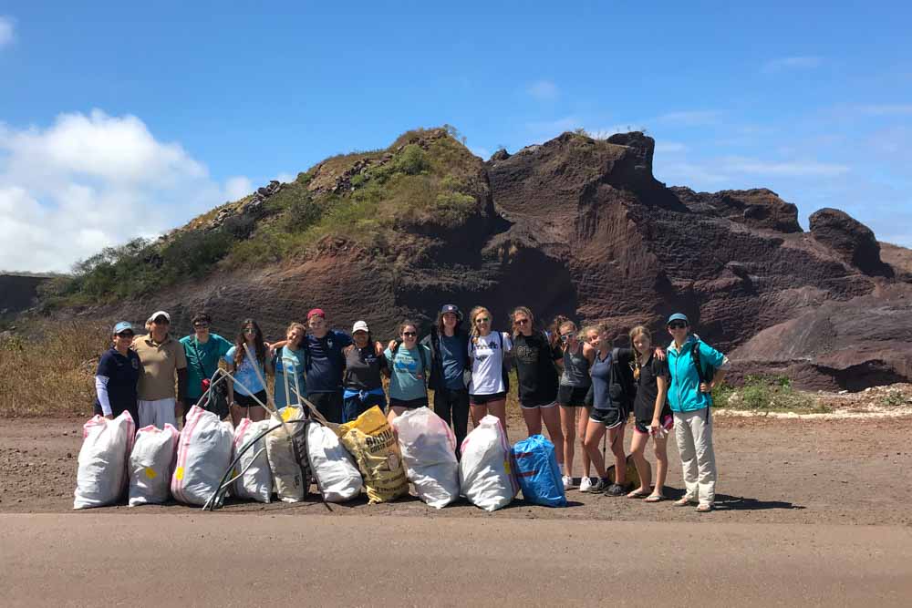 Teen volunteers stand with bags of trash they picked up from the beach during their teen service trip.