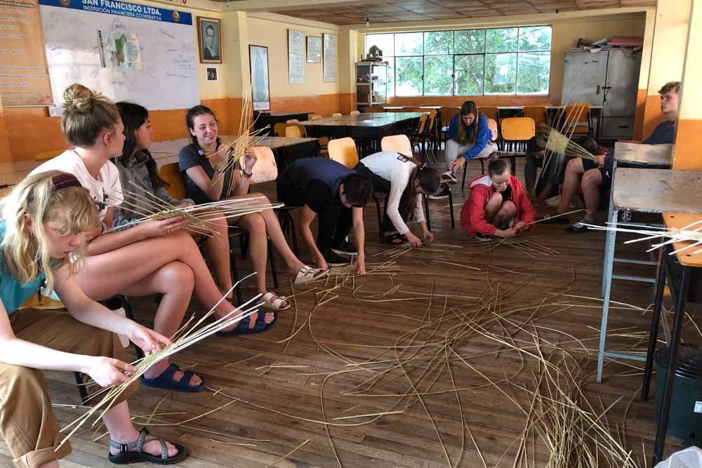 Teens experience cultural immersion by learning traditional basket weaving skills from a community member.