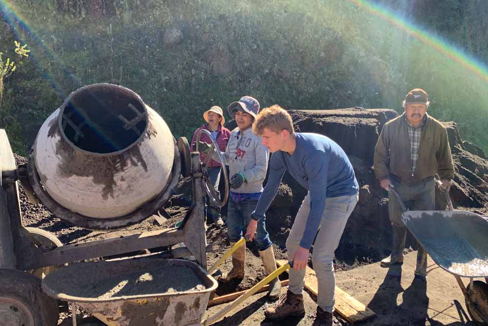 Teens and community members work together mixing cement on a summer service project.