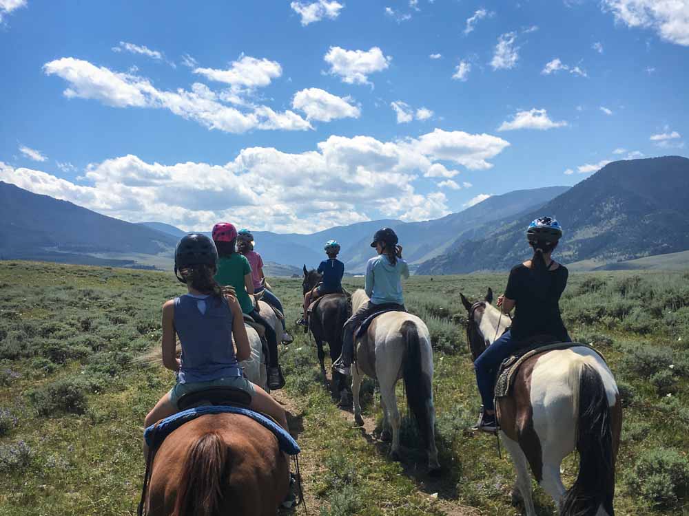A group of teen volunteers rides horses through the Montana landscape.