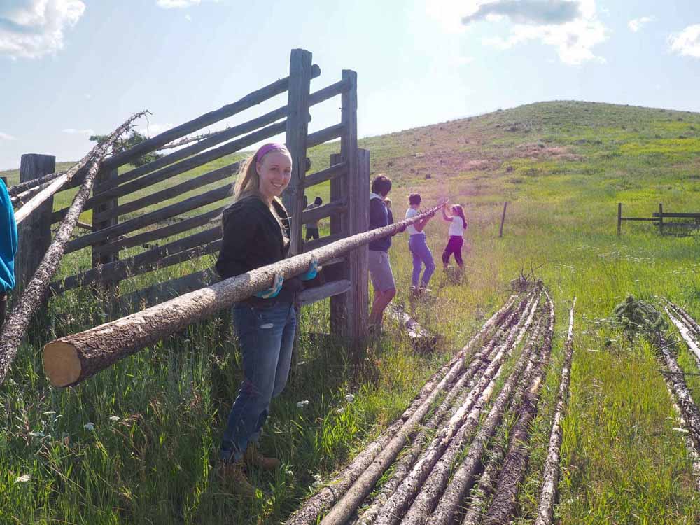 Smiling teen volunteer helps carry teepee poles for summer service project in northwestern Montana.