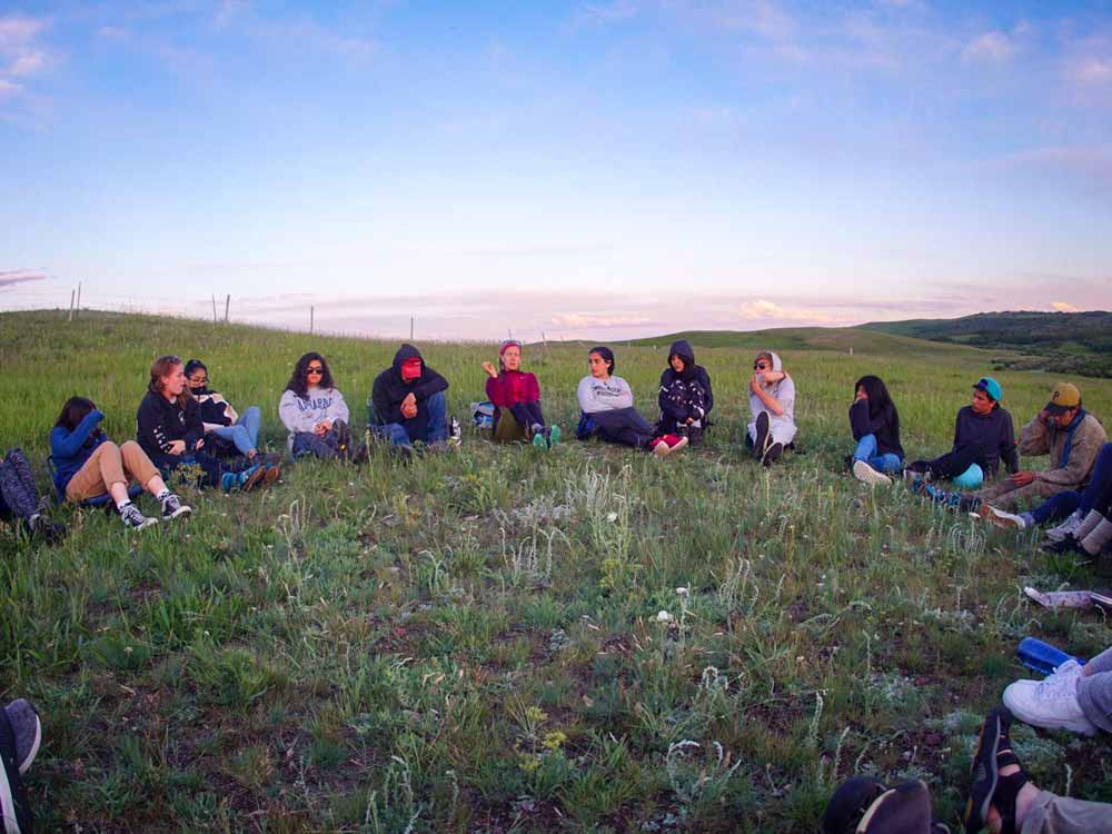 Teen volunteers sit in a circle in the hills of Montana to discuss progress on their summer service projects.