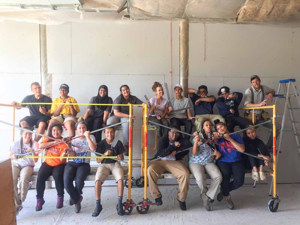 Team of teen volunteers posing for a group photo on the worksite of their summer service project.