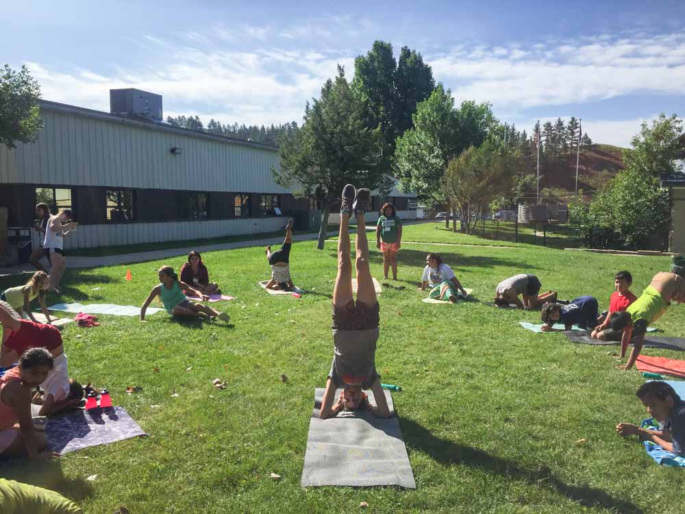 Middle school student doing a hand stand while teaching yoga outside.