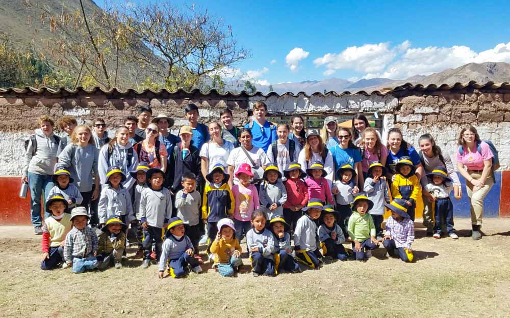 Group of high school volunteers standing with local children in Peru.
