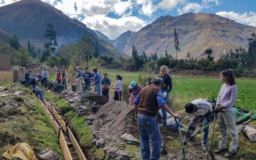A group of teen volunteers digs trenches on a Peru summer service trip with mountains in the background.