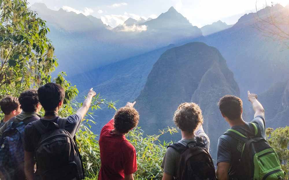 Group of hikers point at sunrise at Machu Picchu on Peru summer service trip.