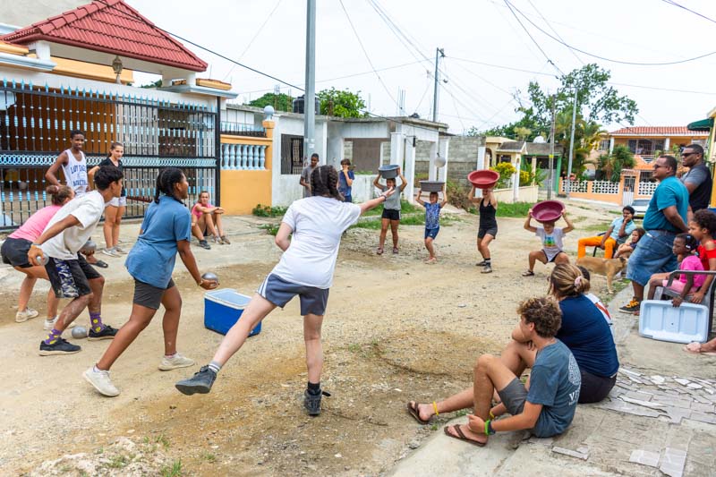 High School Volunteers play game in the street with local kids in the DR as leaders working their dream jobs look on