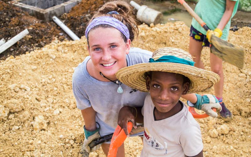 High school volunteer smiles with child as the hold shovels in the Dominican Republic