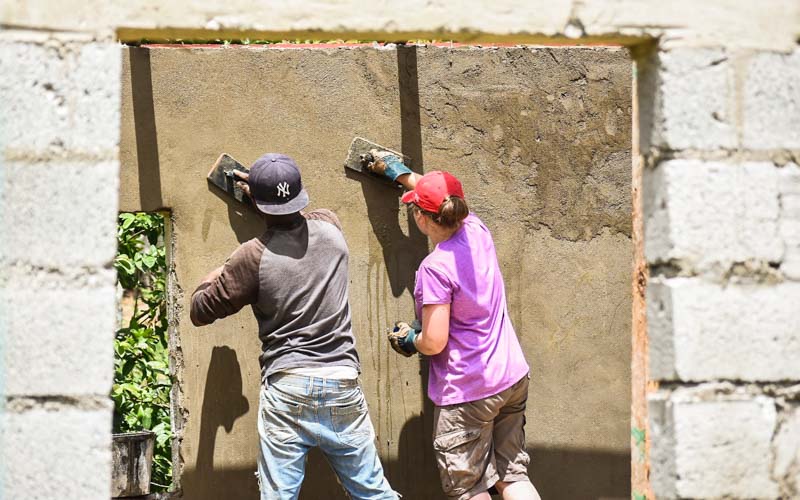 Two teen summer service program high school volunteers smooth out the surface of a stucco wall in the Dominican Republic