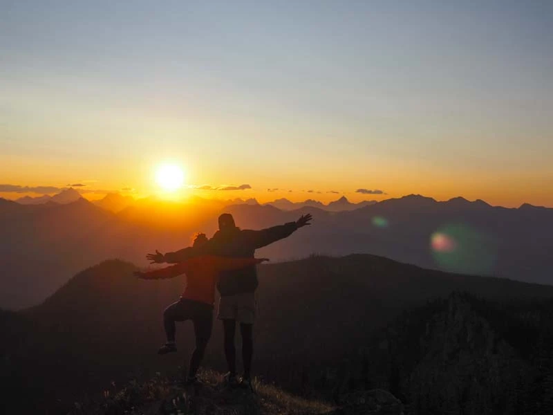 Two college students stretch out their arms on a mountain at sunset during a VISIONS Gap Year program