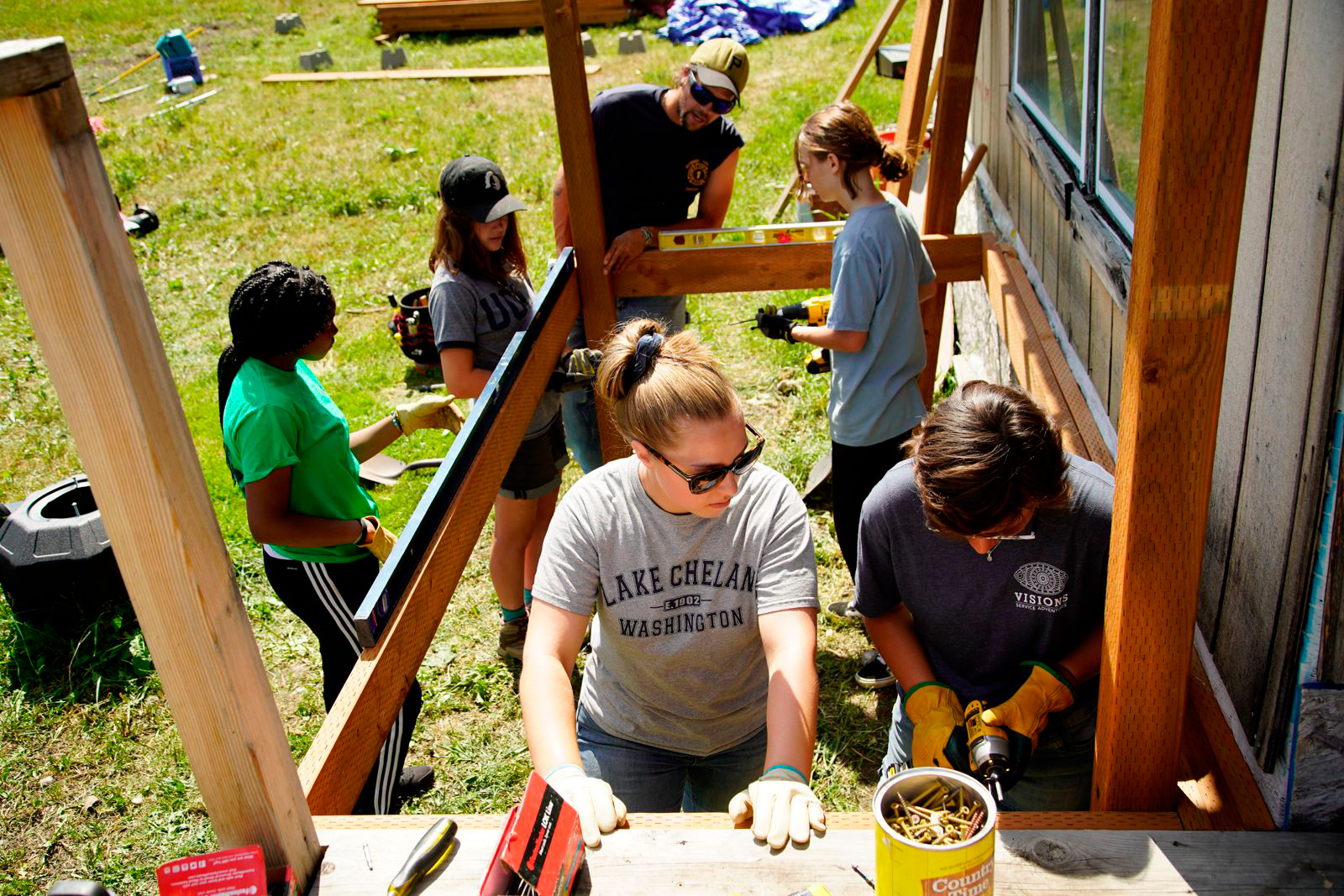 Teens working together outdoors on a construction project, measuring and drilling wooden beams beside a building during a service activity - VISIONS summer