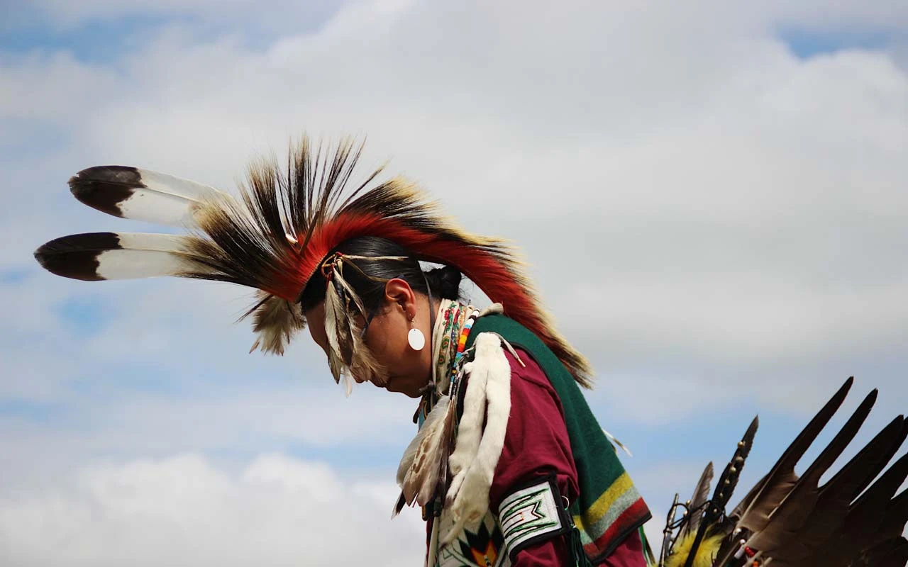 A Blackfeet Native American man with head down in a head dress