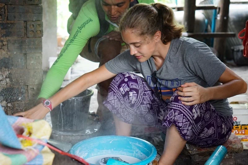 Girl reaching out right arm making paper in Cambodia