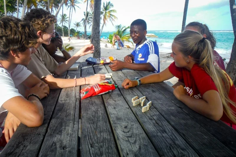 high school students playing dominoes with islander, practicing ways to be more than a tourist