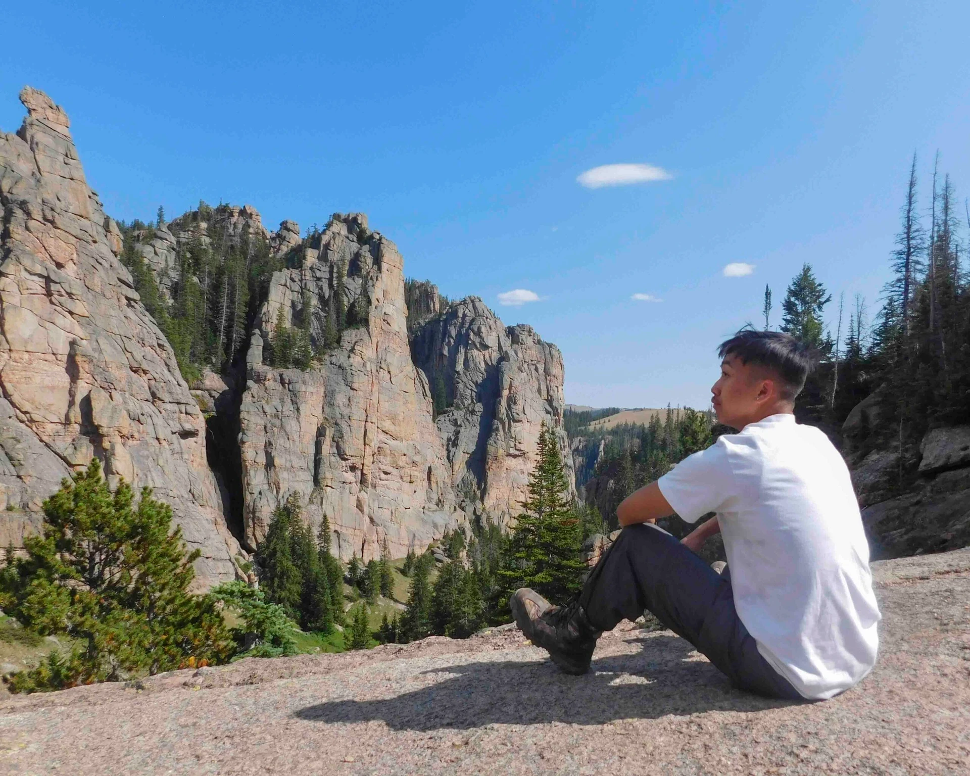 teenage boy sits on large rock slab and looks out at cliffs on community service trips to the Northern Cheyenne