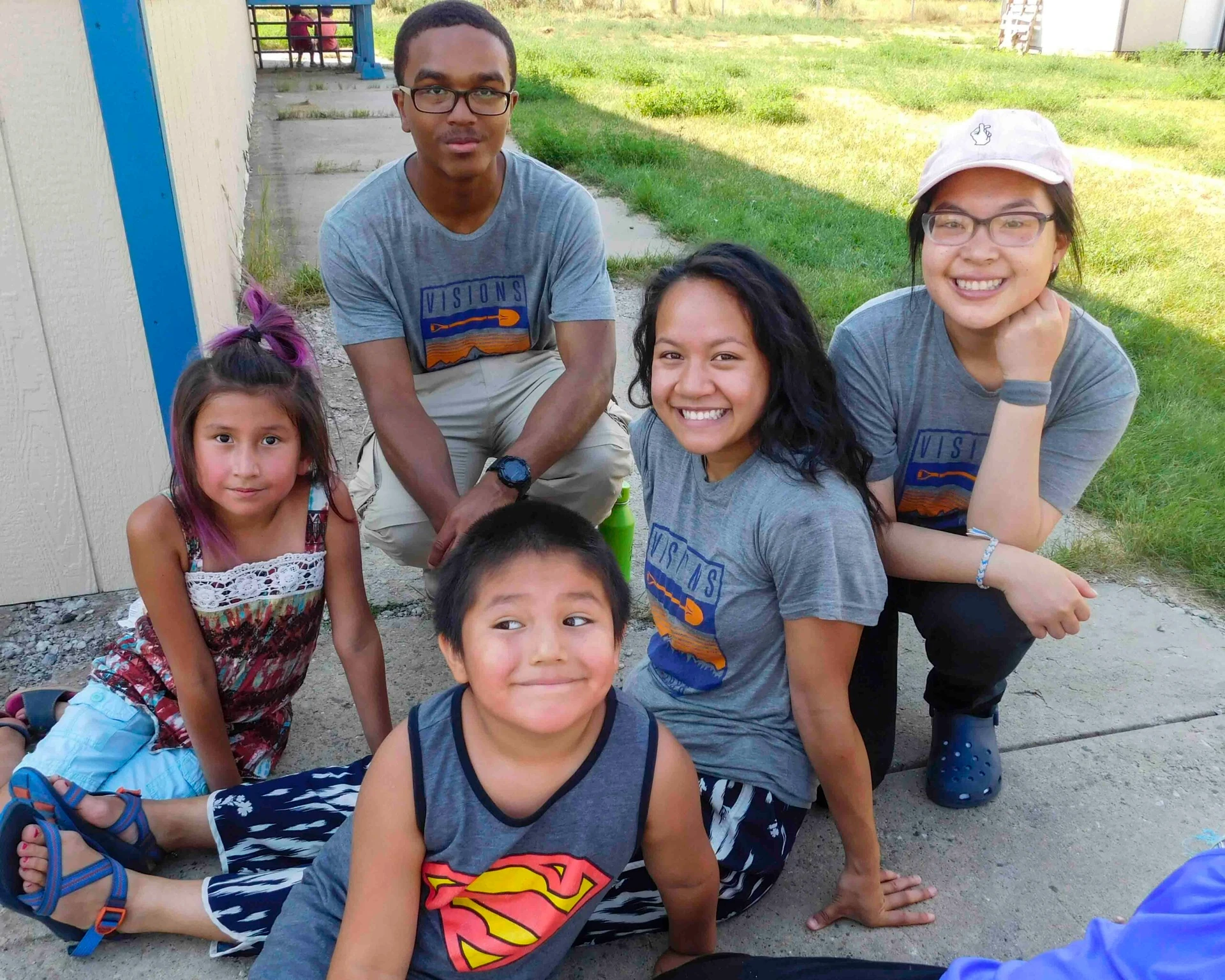 Teen volunteers sit in the shade with local kids on community service trips to the Northern Cheyenne