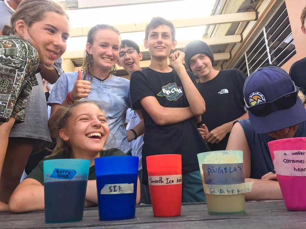 Kids laugh as they stand behind row of smoothies