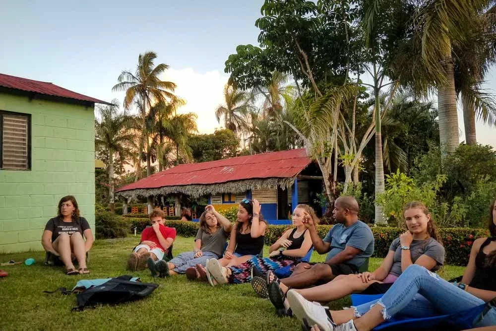 Teen volunteers and program leaders talking near palm trees and colorful houses.