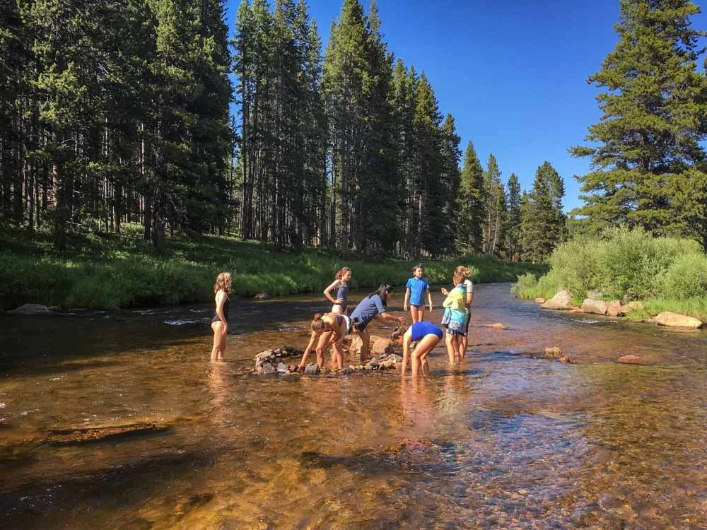 Group of teen volunteers cools off in a river surrounded by forrest.