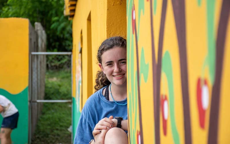 Female teen volunteer smiles next to mural art in the Dominican Republic