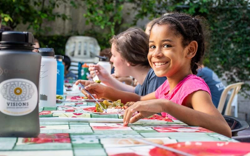 Young girl smiles while eating lunch at a picnic table with international high school volunteers in the Dominican Republic